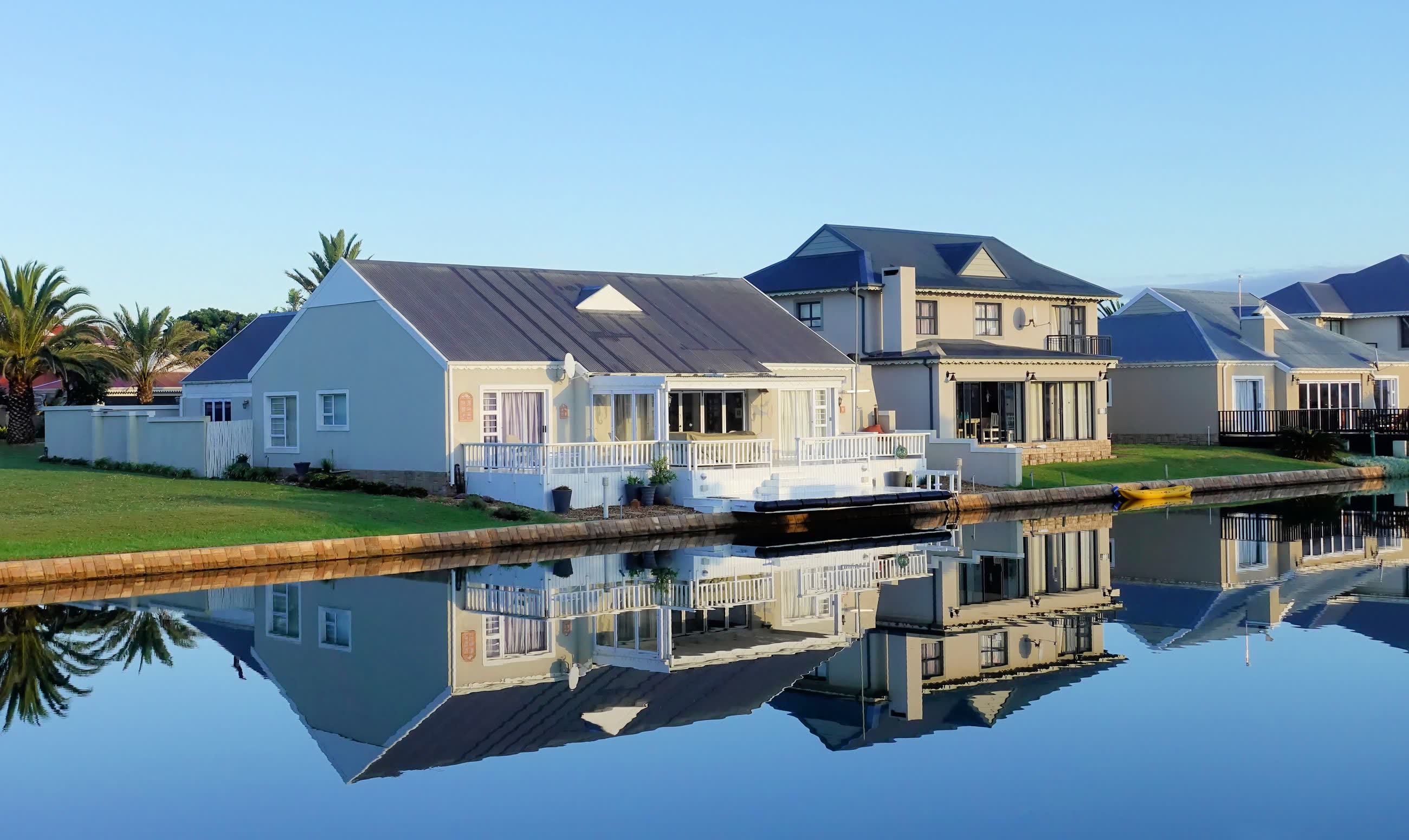 Single-storey waterfront homes lining a still canal, mirrored in the water under a bright blue sky