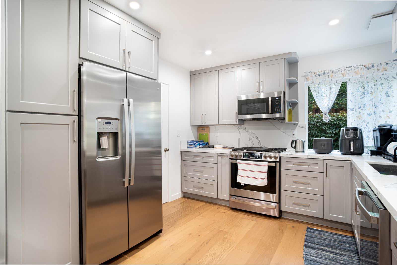 A finished kitchen remodel with pale shaker cabinets, stainless appliances and a light wood floor
