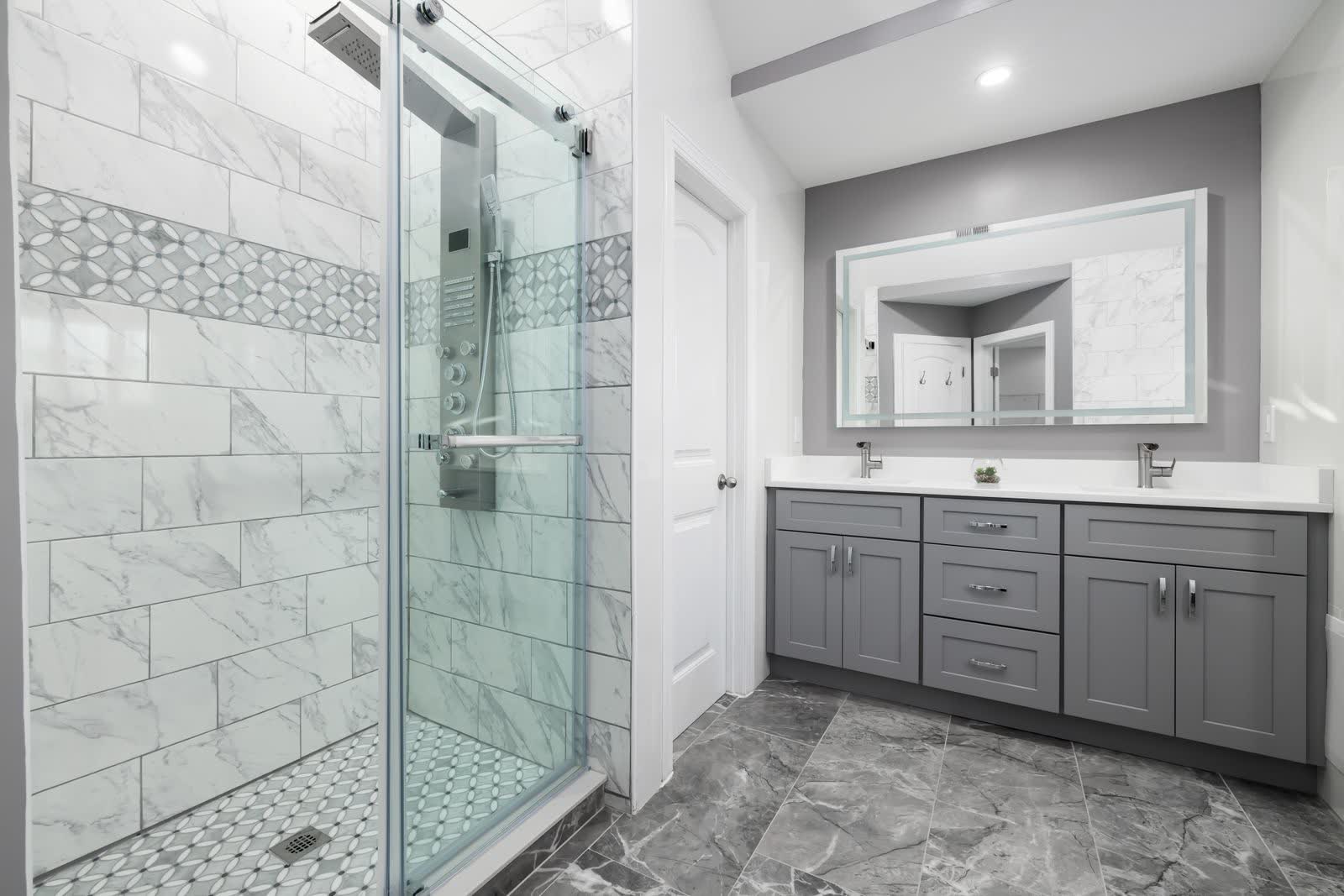 A finished bathroom remodel with a marble-tiled shower, glass door and a grey double vanity