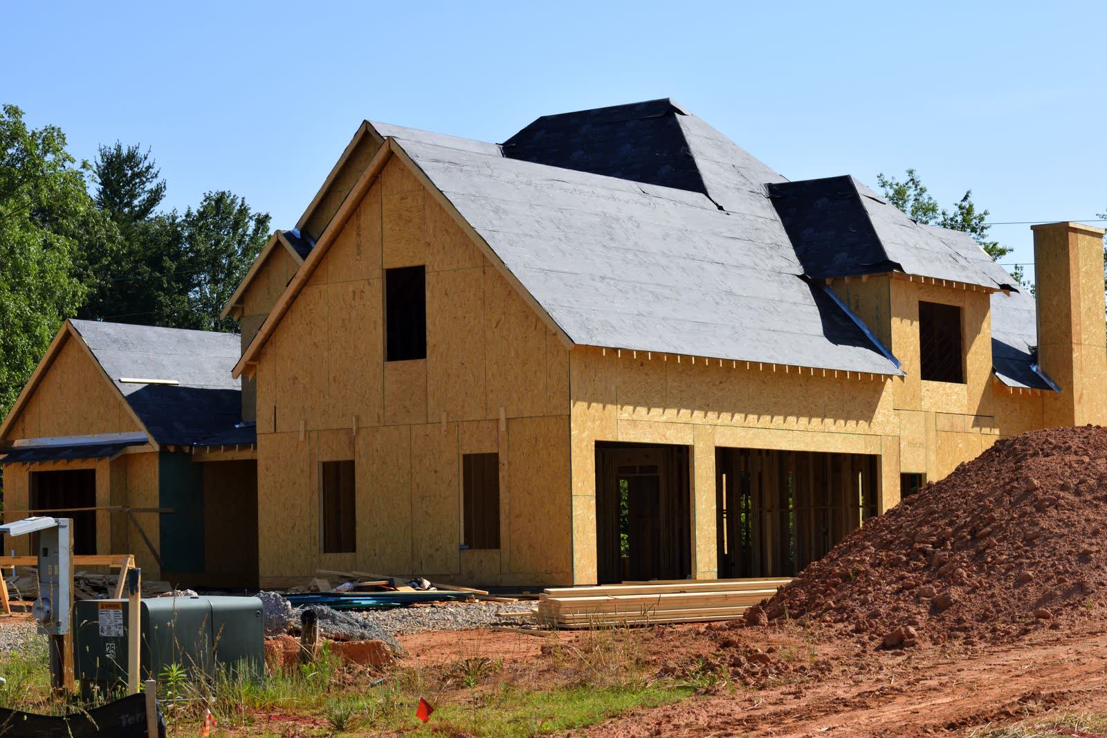 A house framed in fresh lumber with the roof sheathed, standing against a clear blue sky